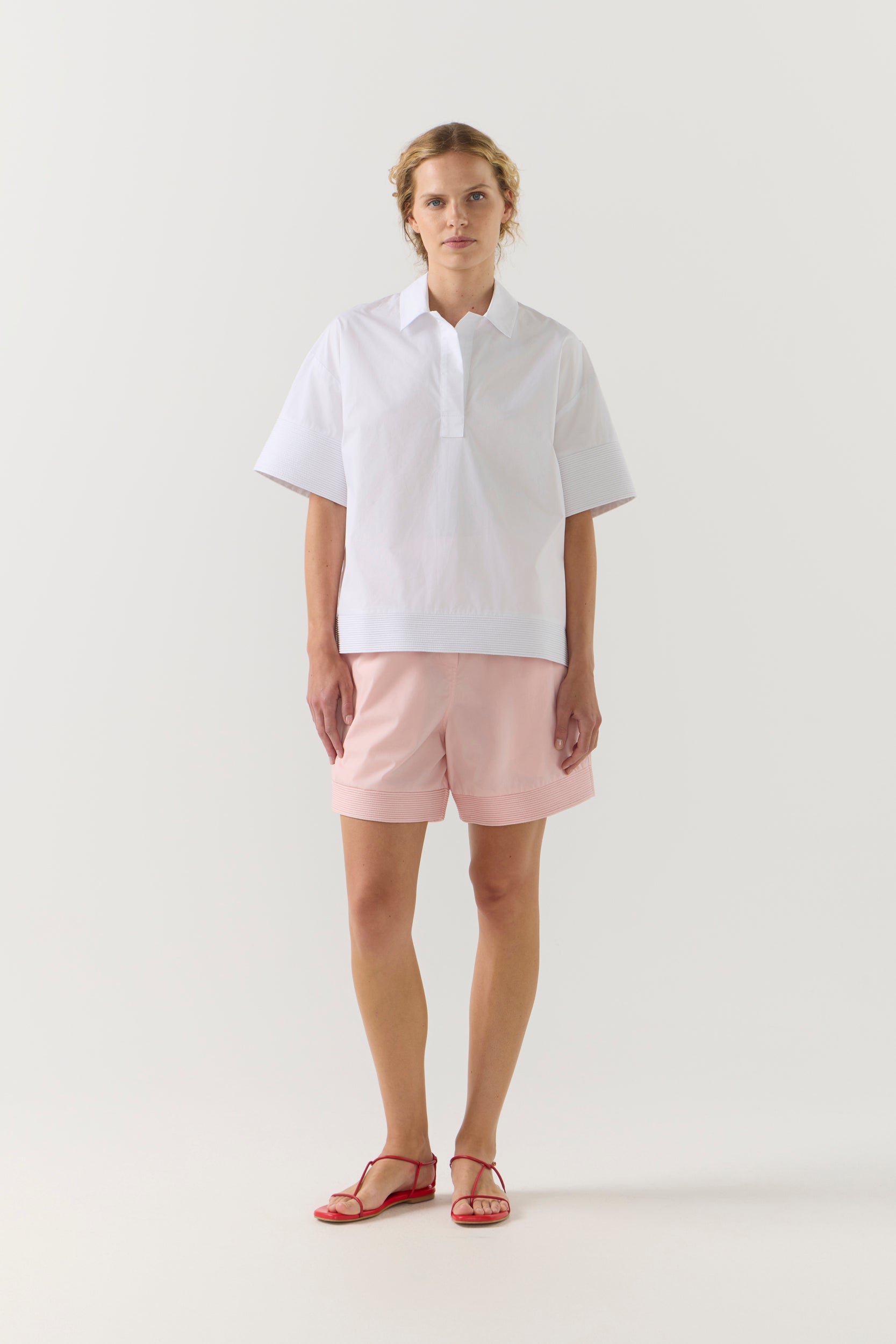 Woman wearing a white shirt and pink shorts on a white background