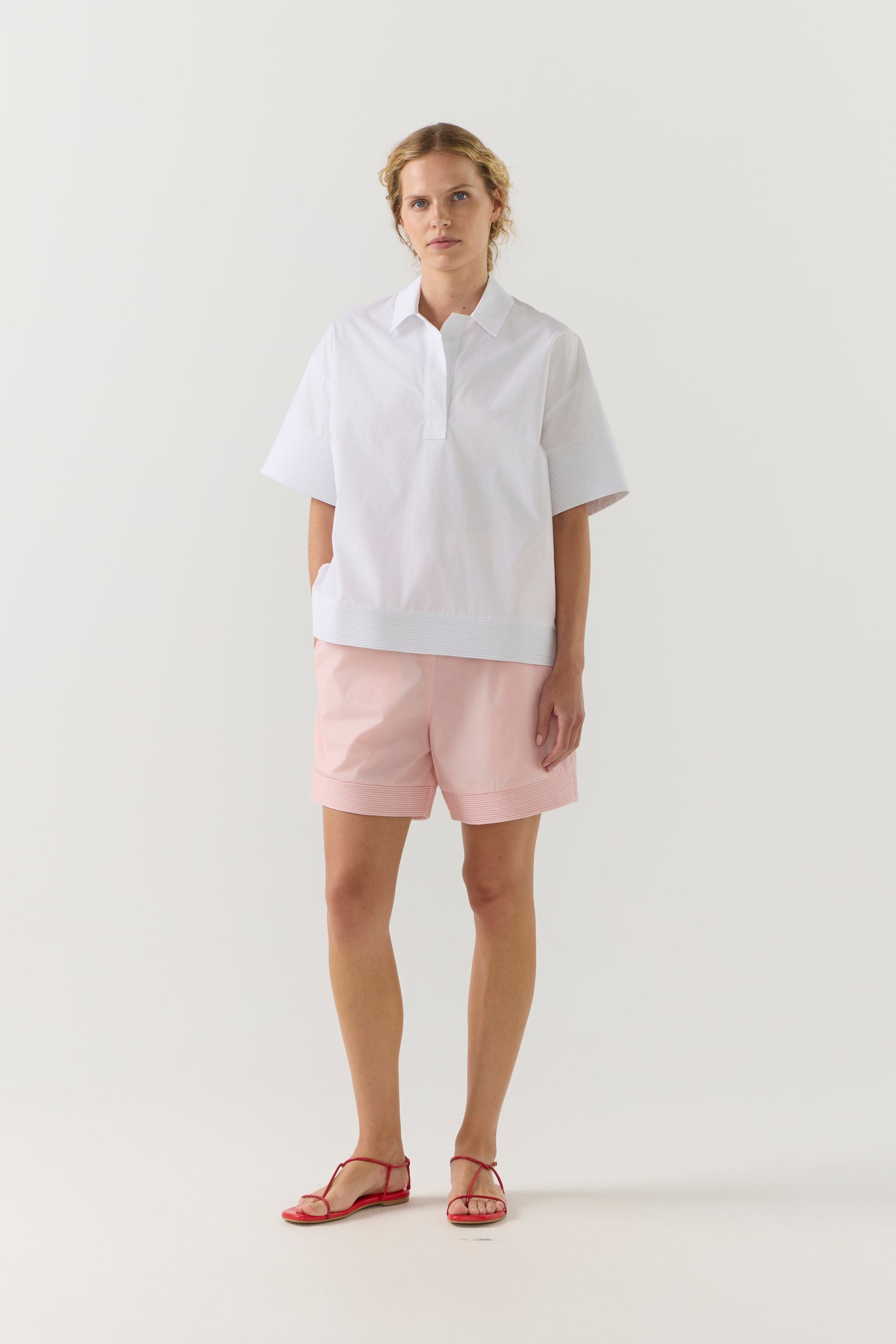 Woman wearing a white shirt and pink shorts on a white background