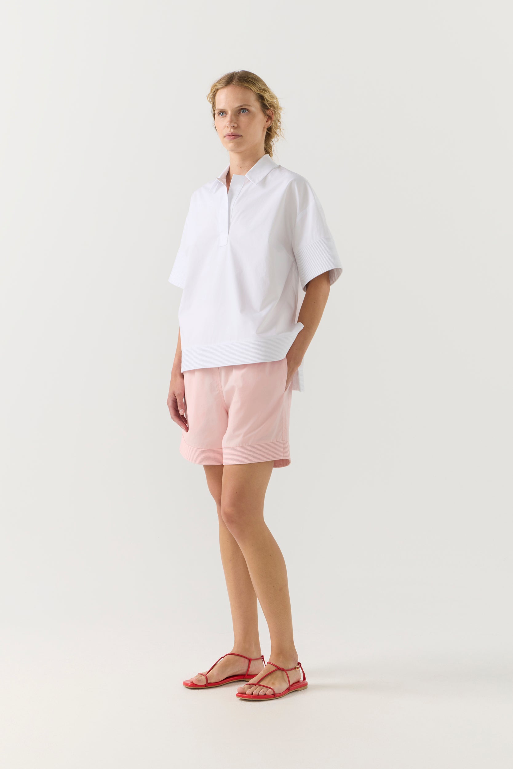 Woman wearing a white shirt and pink shorts on a white background