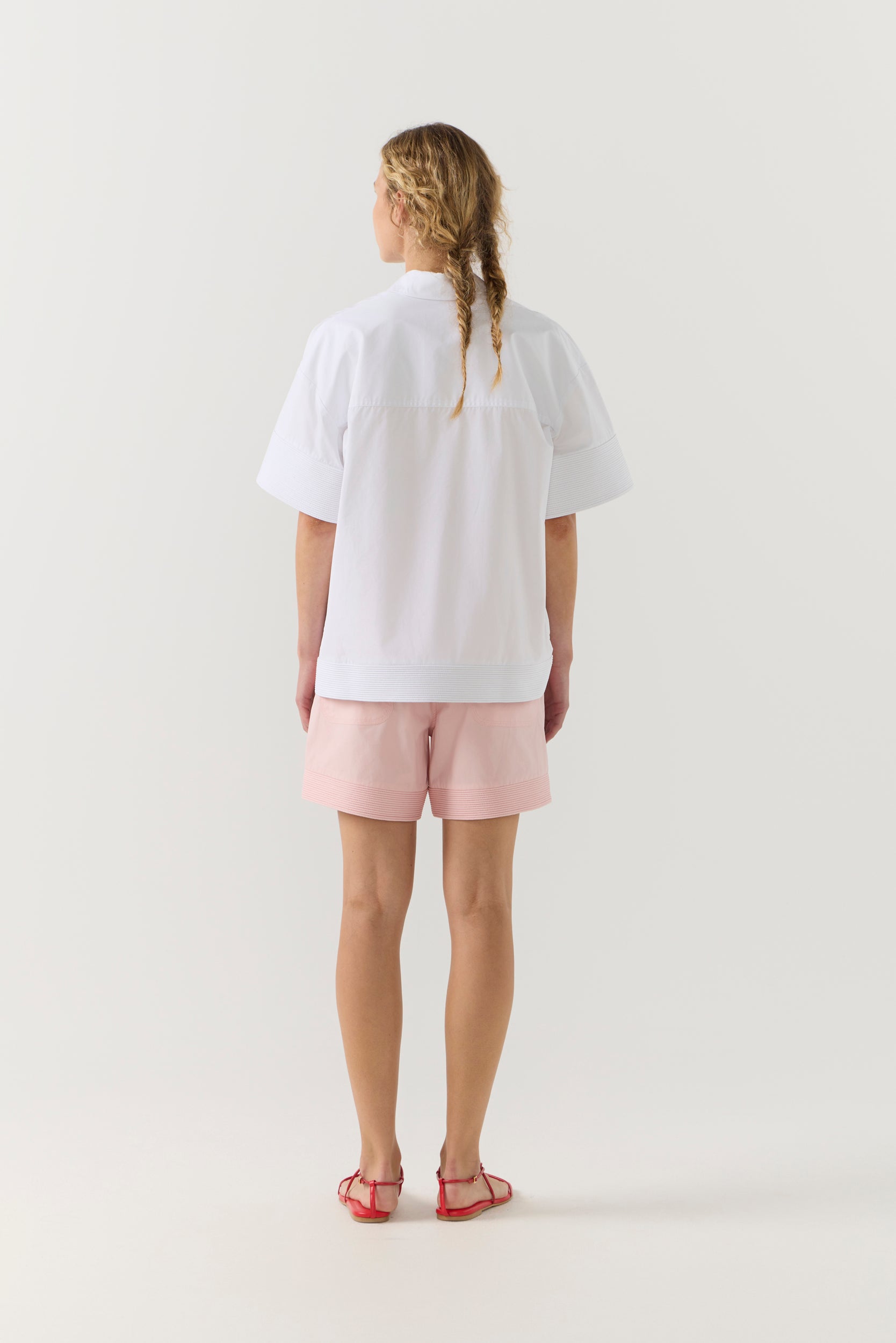 Woman wearing a white shirt and pink shorts on a white background