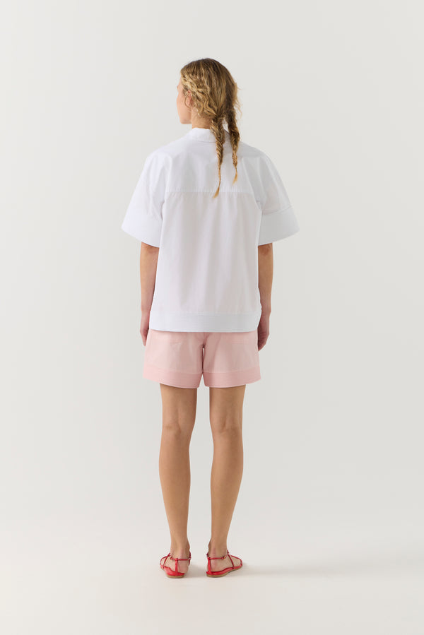 Woman wearing a white shirt and pink shorts on a white background